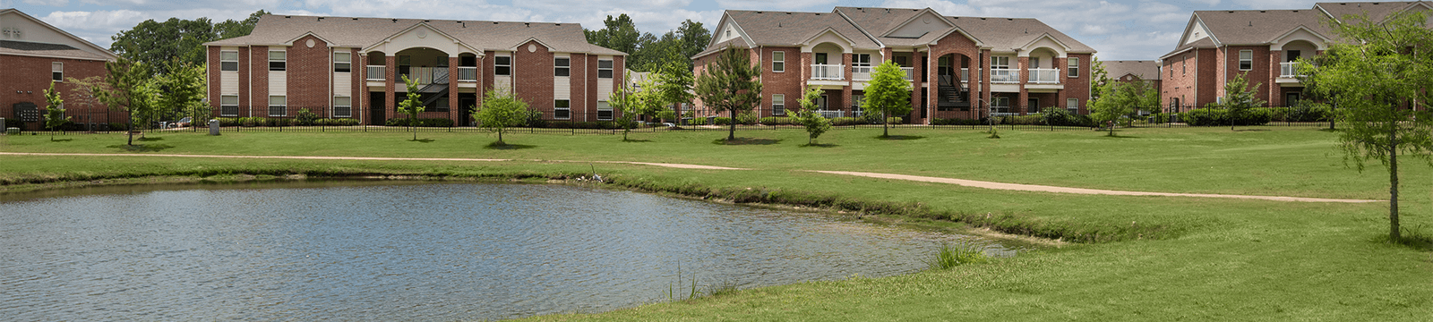 a grassy area with a pond and apartment buildings in the background